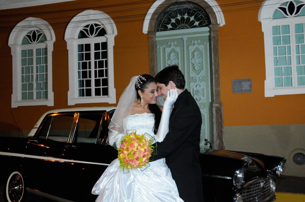 fotografia de casamento, com noivos ao ar livre em momento romântico, com carro antigo ao fundo na frente de uma casa colonial